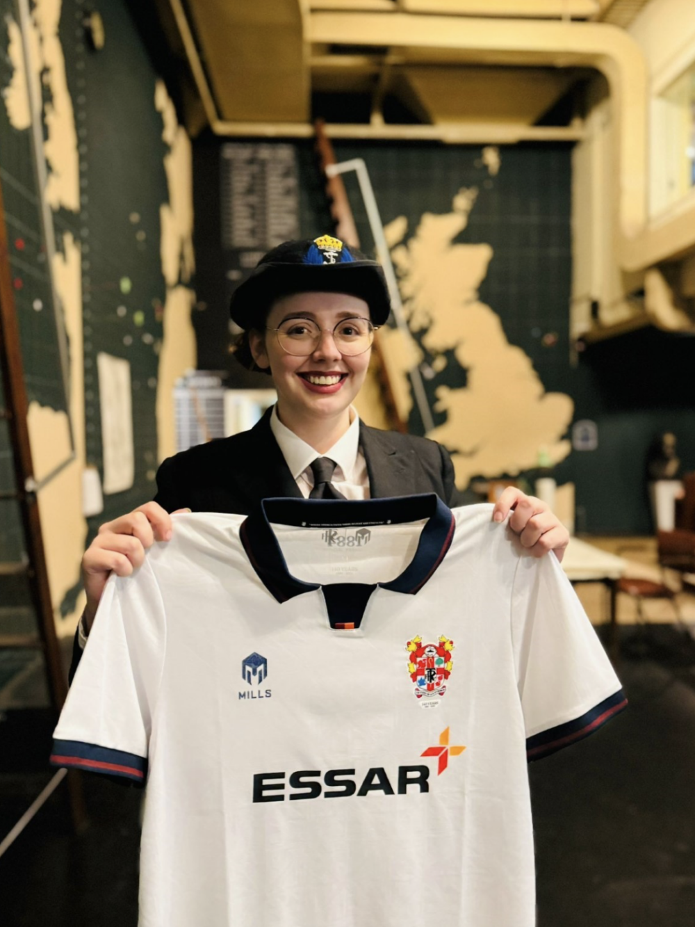 Western Approaches Staff member Lauren in Wrens Uniform holding a Tranmere Shirt in the Operations Room. Credit: Western Approaches