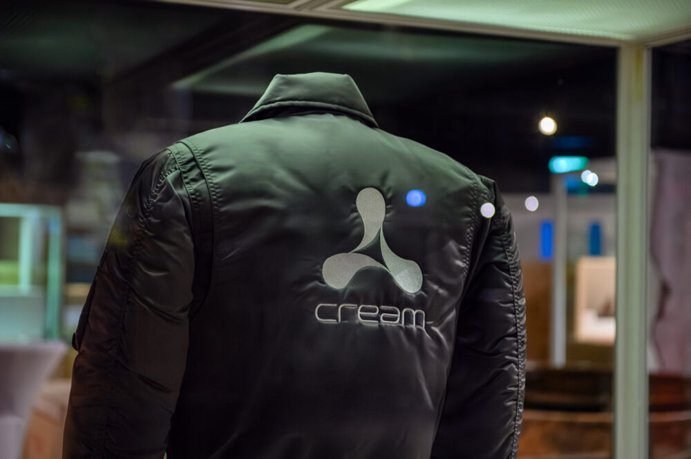 A black bomber jacket with the "Cream" logo, photographed at an exhibition launch event.