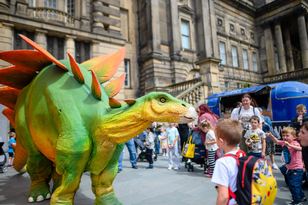 A large dinosaur costume interacts with children at the Dinomania event outside the World Museum Liverpool.